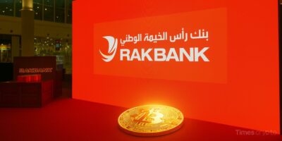 a gold coin with a lit up sign behind it. RAKBANK Makes History as First UAE Bank to Offer Retail Crypto Trading